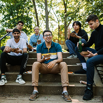 Six students sitting on an outside stairs eating