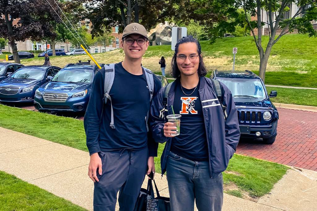 Two students standing on the sidewalk smiling.