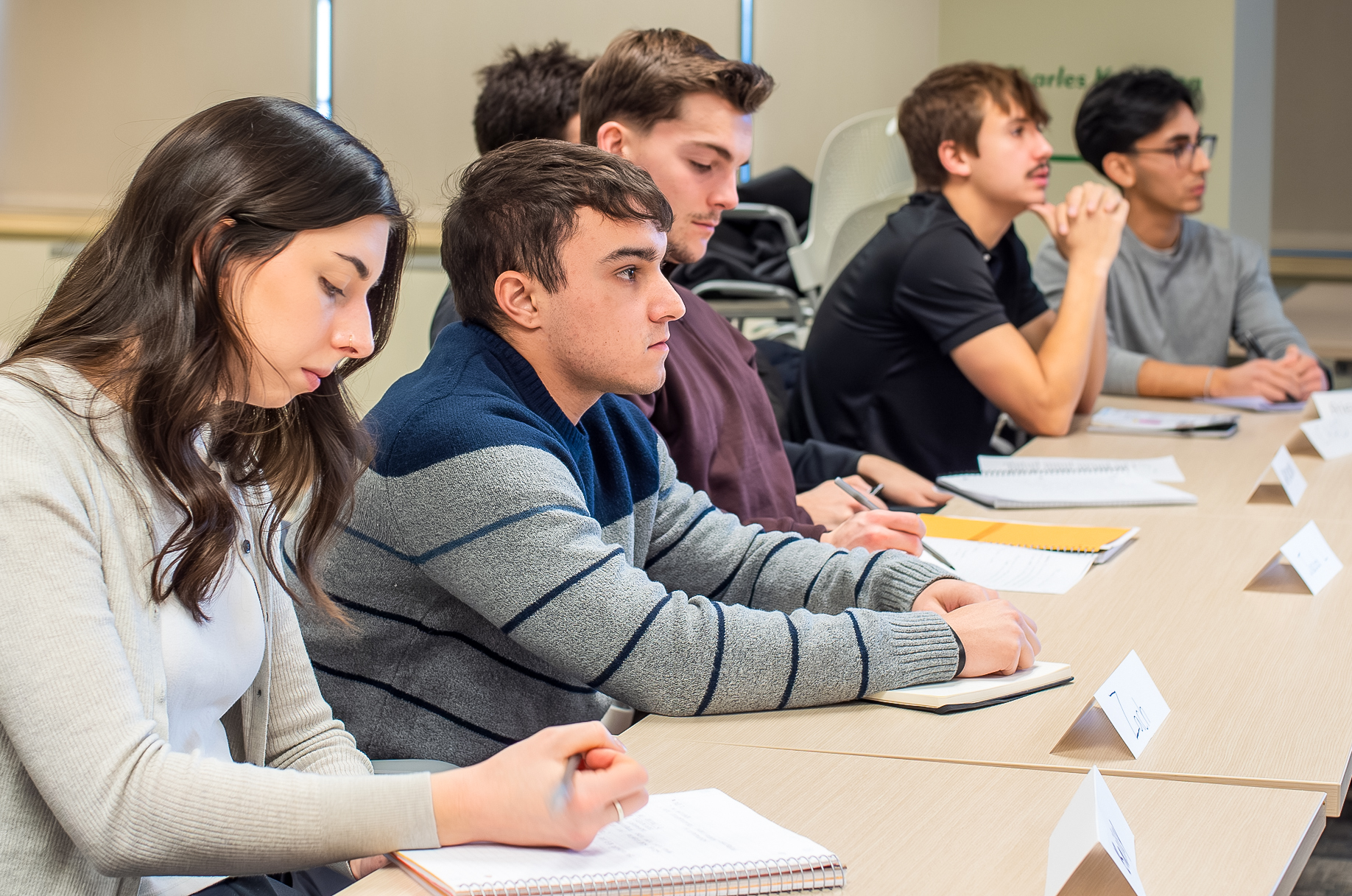 Five students at a table listening to a speaker.